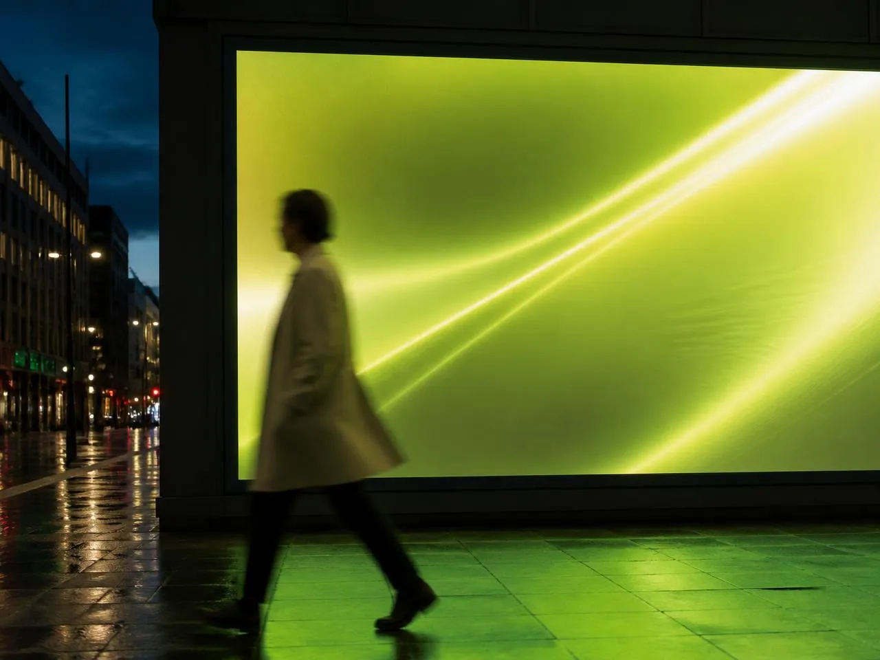 Pedestrian walking past a large glowing digital billboard at dusk