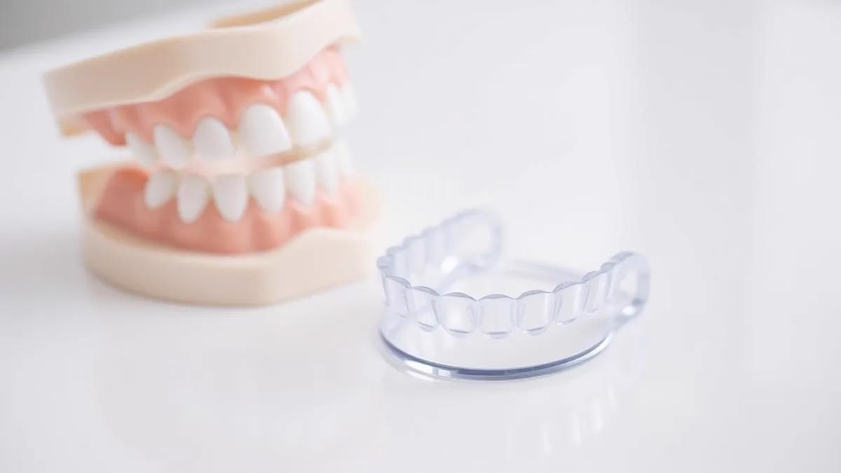 Clear dental aligner tray beside a dental model on a white surface